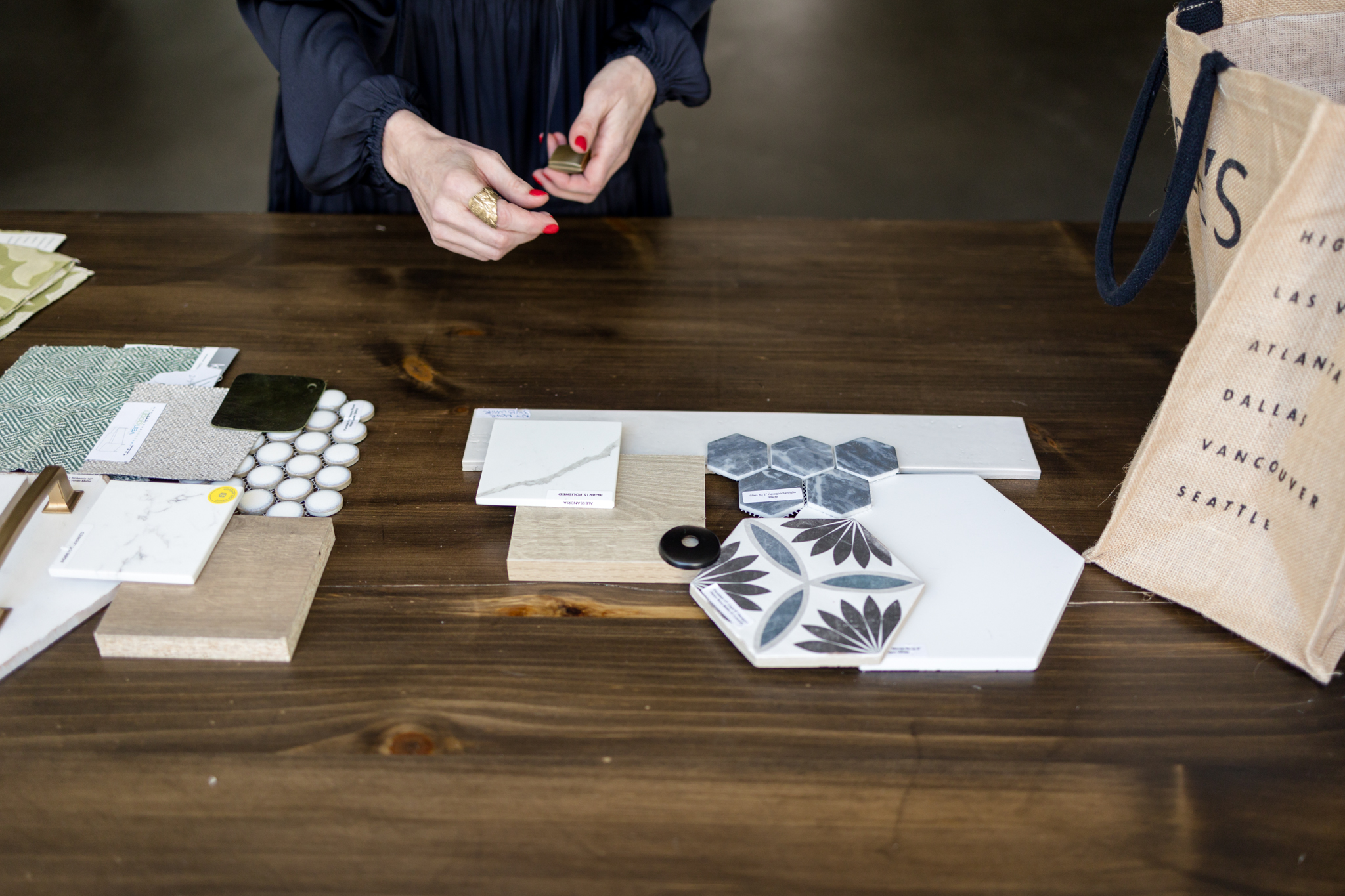 Hands of a project manager arranging tile, fabric, and hardware samples on a wood table, reviewing design materials for a renovation.