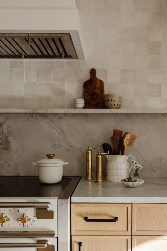 Kitchen detail with marble backsplash, wood utensils in ceramic jar, and brass accents.