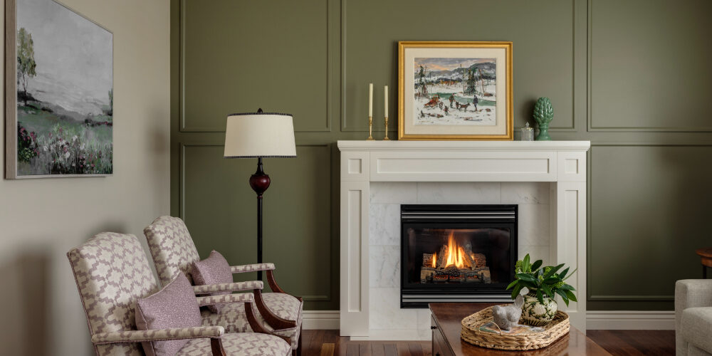 Cozy living room with green accent wall, white fireplace, patterned chairs, and wall art—classic interior design trends.