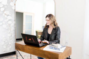 Interior designer working at laptop, researching design trends in a modern, light-filled home office.