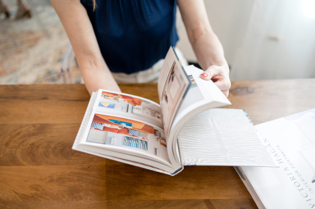 Designer flipping through a lookbook of interior design trends at a wood desk.