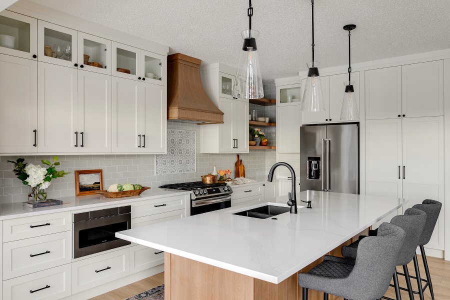 Modern white kitchen with shaker cabinets, a large island, wood accents, stainless appliances, and pendant lights creating a clean, airy feel.