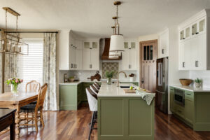 Warm kitchen with green cabinetry, spacious island seating, layered lighting, and open connection to the dining area, designed for comfortable everyday living and easy flow.