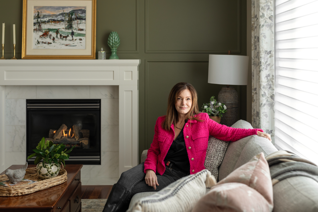 Inviting living room with fireplace and seated woman, layered textiles, and soft lighting, showing a comfortable, well-designed space meant for relaxed daily living.