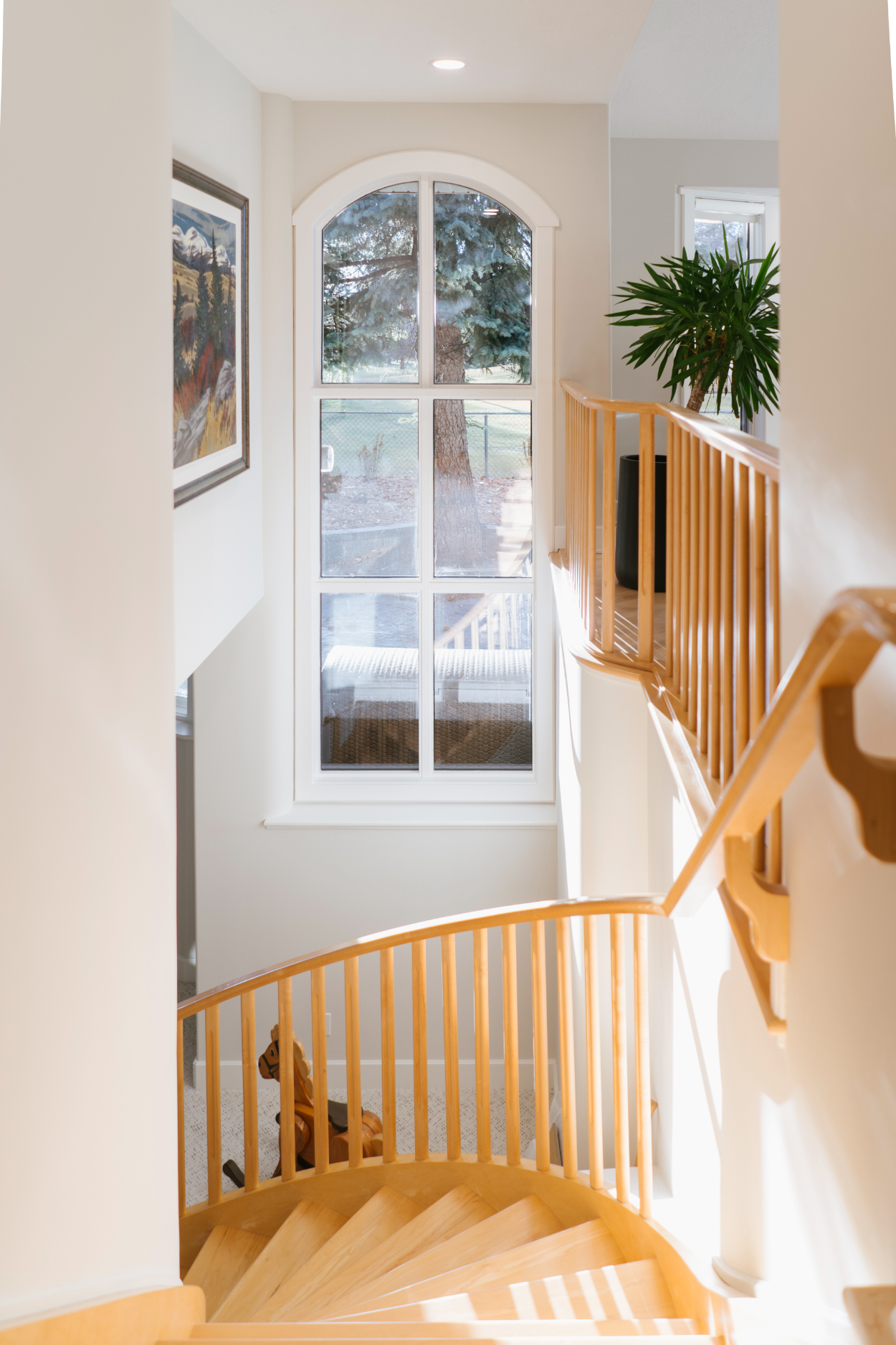 Staircase view from Varsity Estates home renovation with natural light, wood railing, and bright walls.