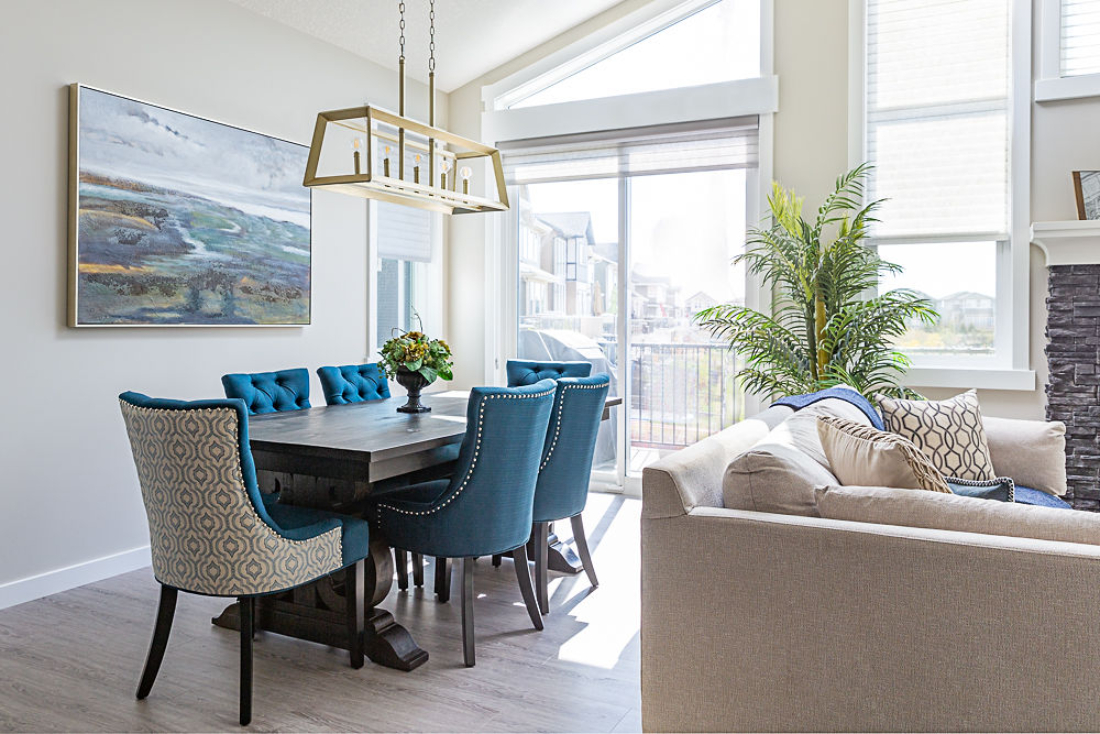 Bright dining area with tufted blue chairs, wood table, and statement chandelier. Natural light and layered textures create a warm, inviting atmosphere.