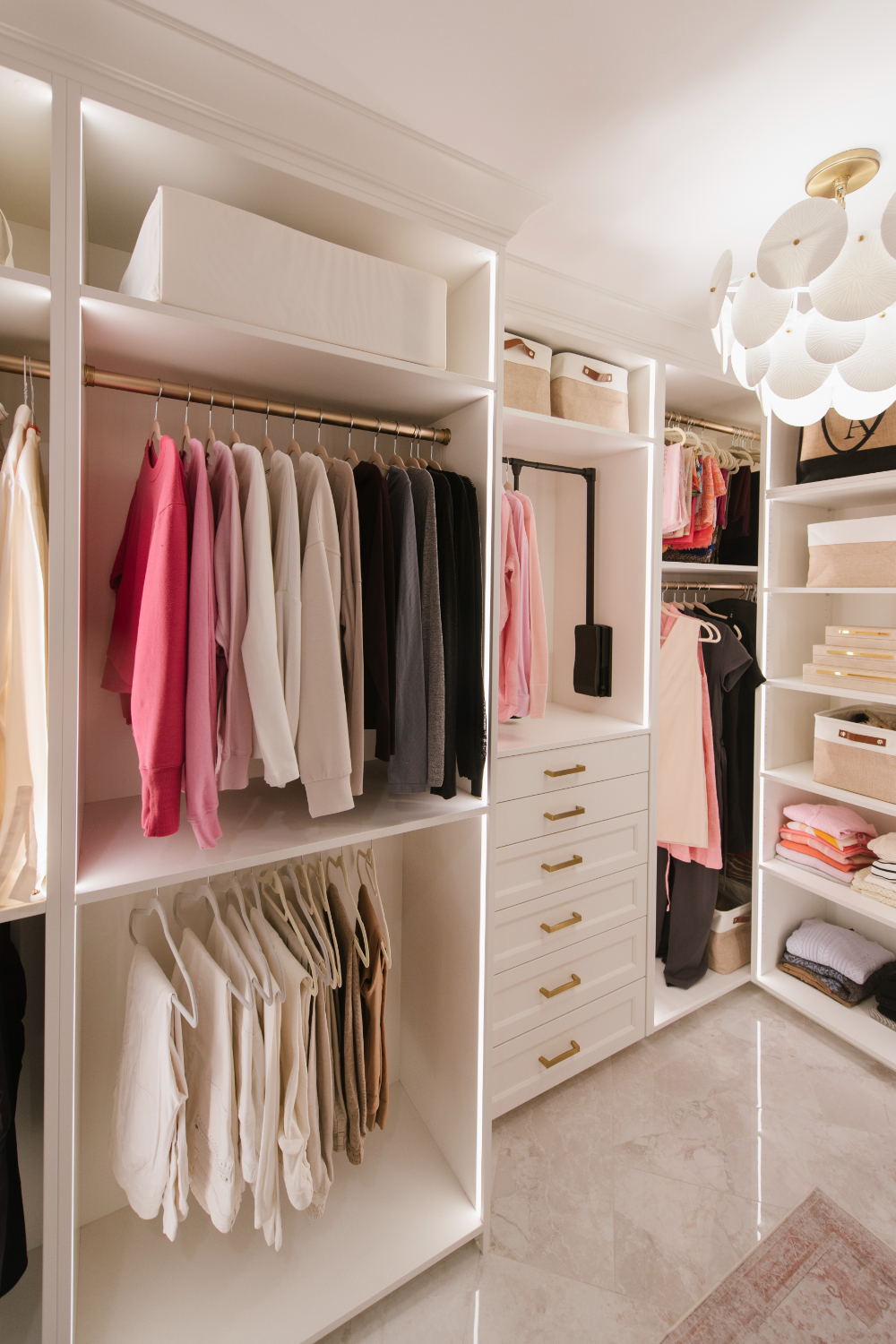 Organized walk-in closet with soft lighting, neutral tones, and neatly arranged clothing, showcasing polished storage design in the context of interior decorator vs interior designer.