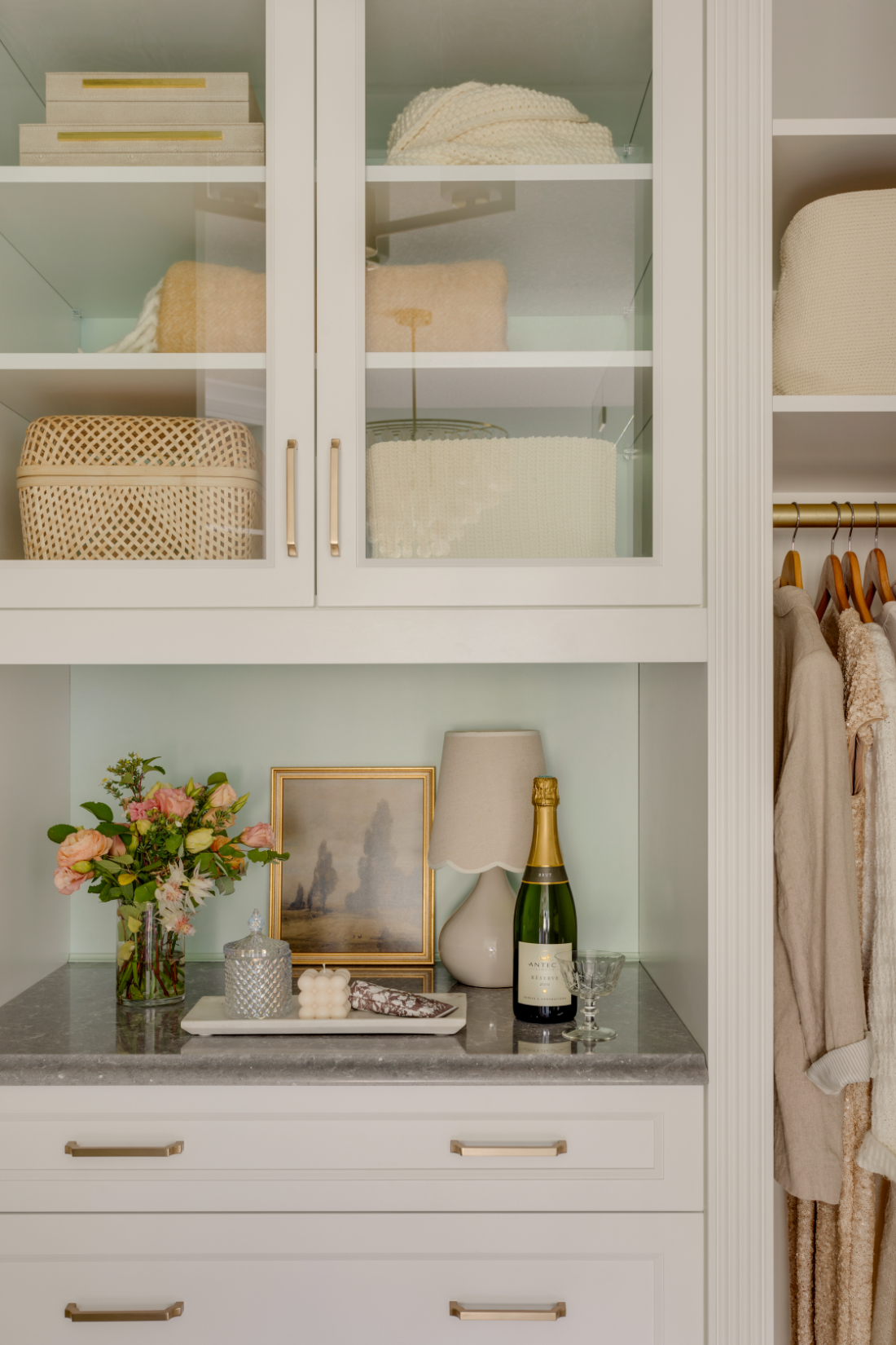 Custom white built-in closet with glass cabinet doors, brass hardware, and styled open shelving in a Room Service Interiors home design.